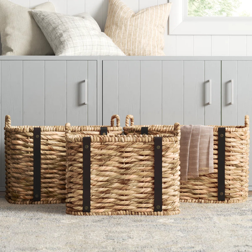 Three wicker baskets with brown straps in front of a gray cabinet.
