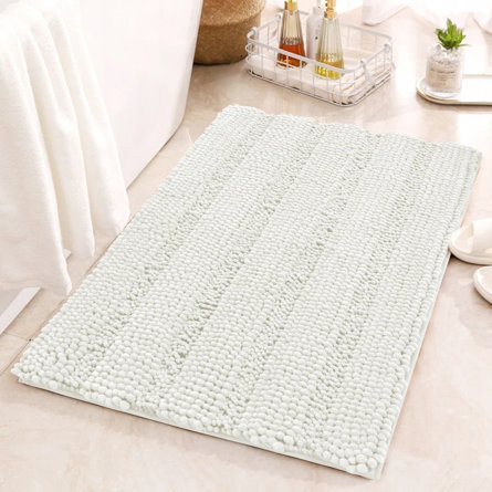White plush bath mat on a tiled bathroom floor.