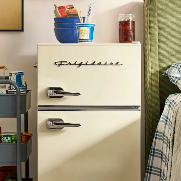 Cream retro-style Frigidaire mini fridge with chrome handles placed next to a be